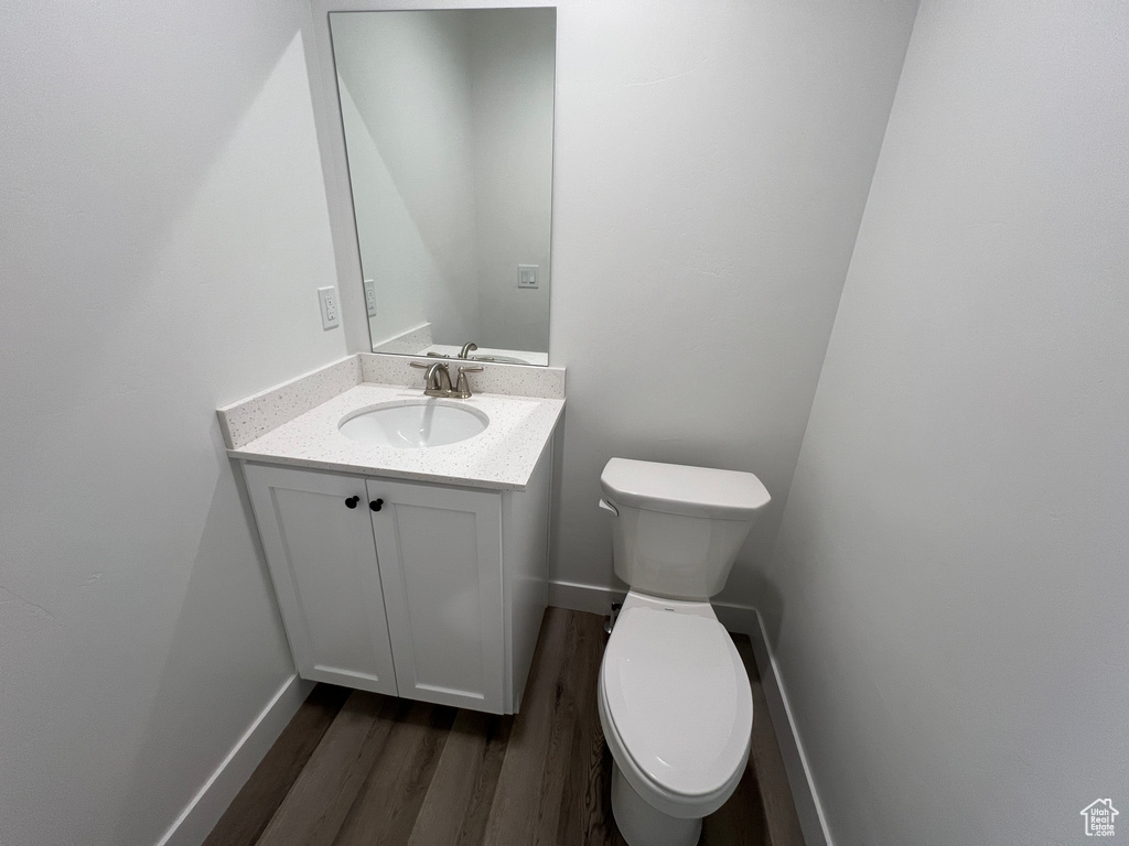 Half bathroom featuring toilet, baseboards, wood finished floors, and vanity