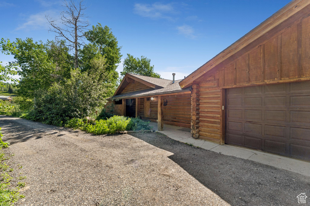 View of front of home with an attached garage, log siding, and a shingled roof