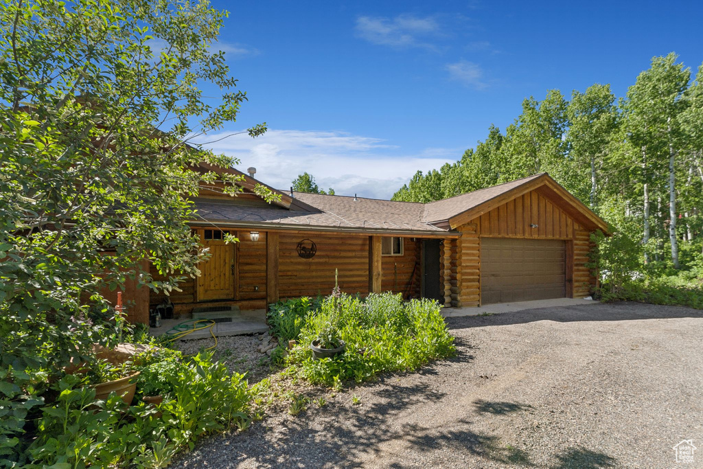 View of front of home featuring a garage, log siding, a shingled roof, driveway, and board and batten siding