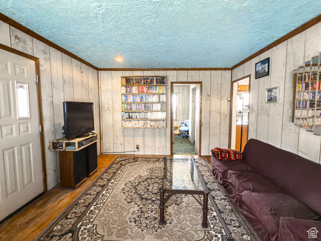 Living room with crown molding, wood finished floors, wooden walls, and a textured ceiling