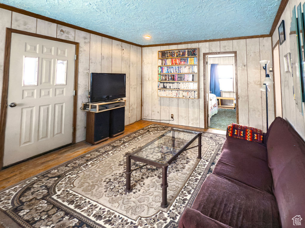 Living area featuring crown molding, a textured ceiling, wood finished floors, and wood walls