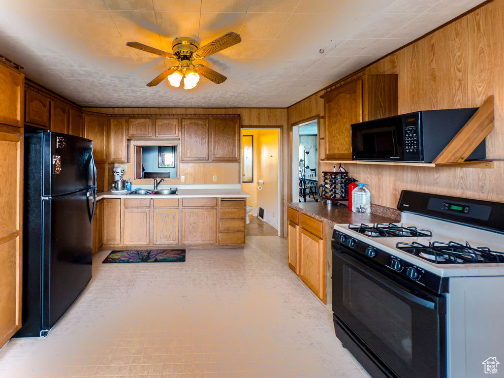 Kitchen with black appliances, a ceiling fan, wooden walls, and brown cabinets