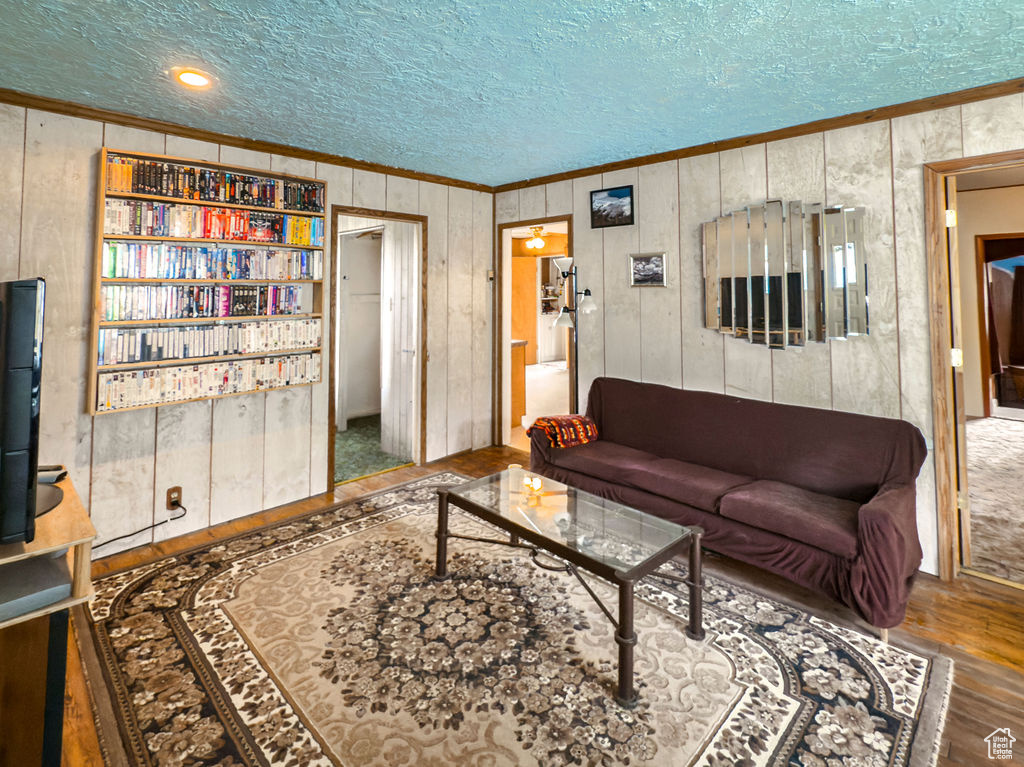 Living room with crown molding, a textured ceiling, wood finished floors, and wood walls