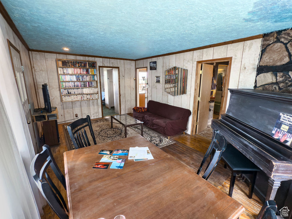 Dining room with ornamental molding, a textured ceiling, wood finished floors, and wood walls