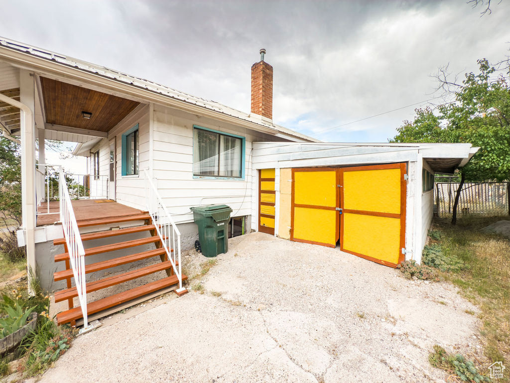 View of property exterior with a chimney, a porch, a metal roof, and a storage shed
