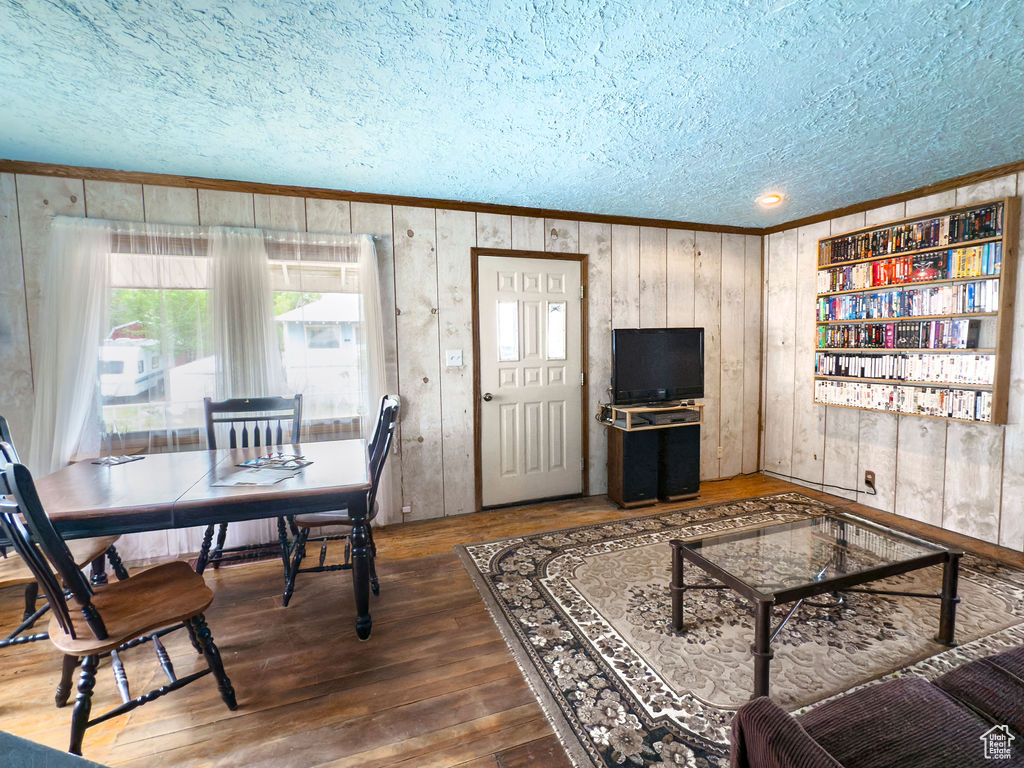 Living room with a textured ceiling, ornamental molding, wooden walls, and wood-type flooring