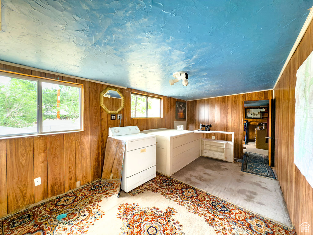 Laundry area featuring wooden walls, light colored carpet, washing machine and dryer, and a textured ceiling
