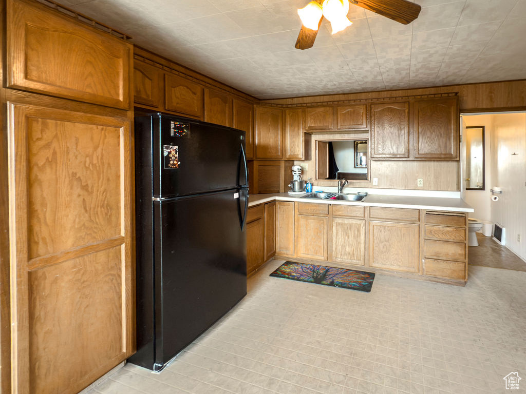Kitchen with freestanding refrigerator, light countertops, a ceiling fan, wood walls, and brown cabinets