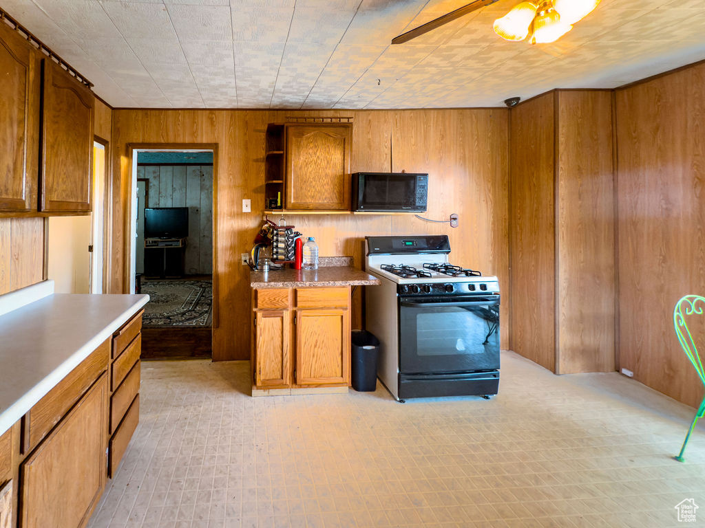 Kitchen with range with gas cooktop, black microwave, wood walls, brown cabinetry, and open shelves