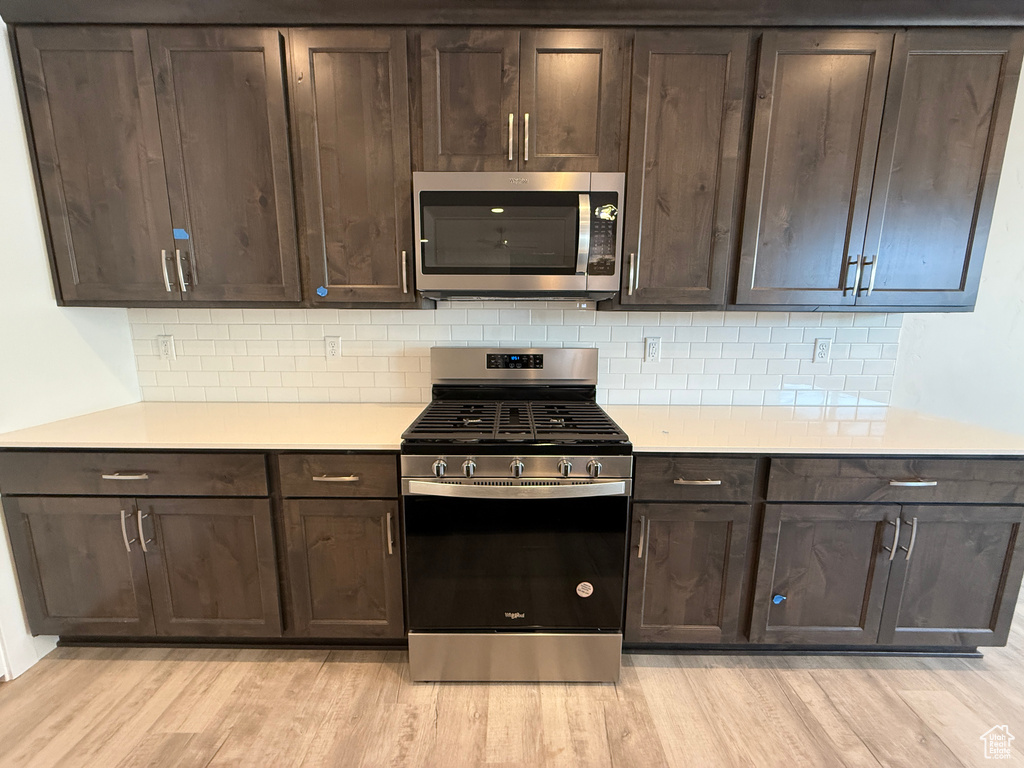 Kitchen with stainless steel appliances, dark brown cabinets, light countertops, and light wood-style flooring