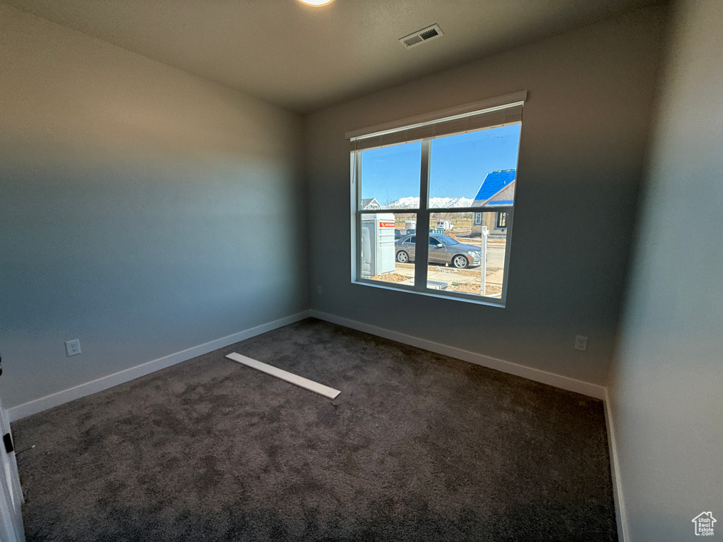 Empty room featuring dark colored carpet, visible vents, and baseboards