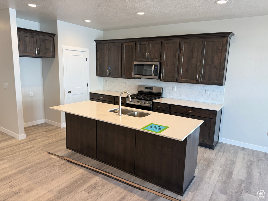 Kitchen with a center island with sink, tasteful backsplash, light countertops, appliances with stainless steel finishes, and a sink