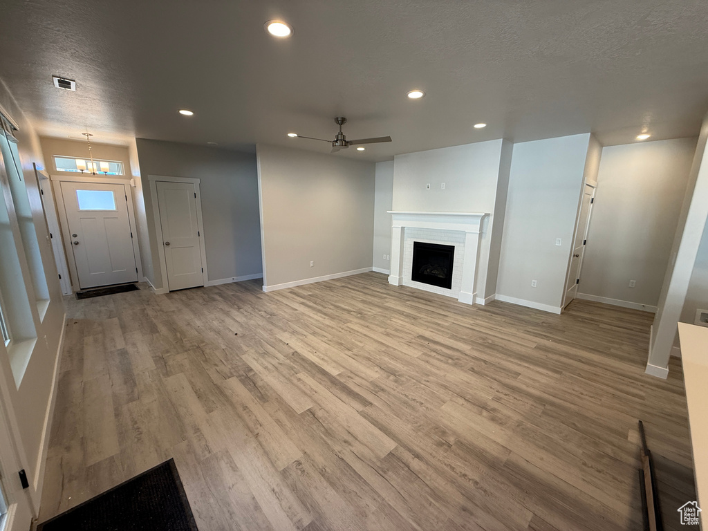 Unfurnished living room featuring a textured ceiling, recessed lighting, a fireplace, baseboards, and light wood-style floors