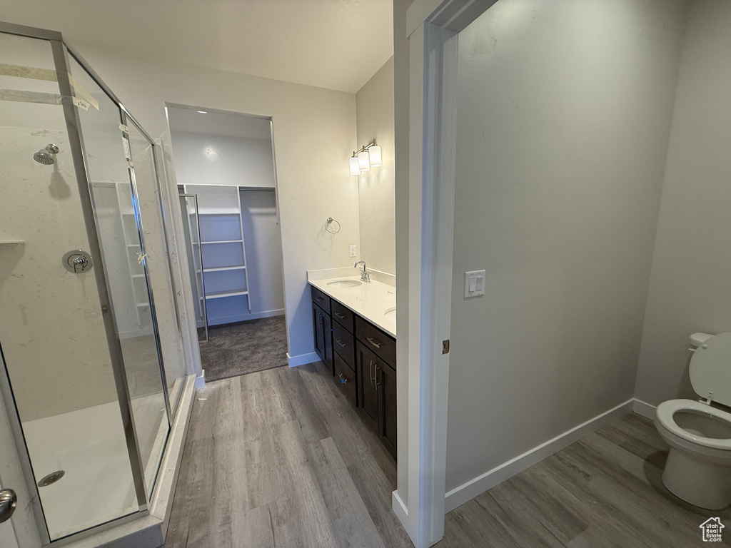 Full bathroom featuring double vanity, a spacious closet, a sink, a shower stall, and wood finished floors