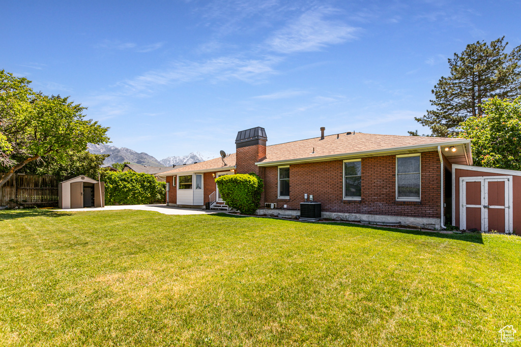 Rear view of property featuring brick siding, central AC, a chimney, and a patio