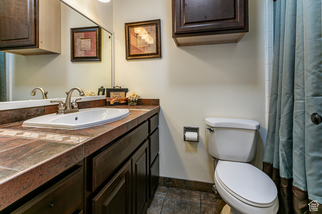 Bathroom with baseboards, toilet, curtained shower, stone finish flooring, and vanity