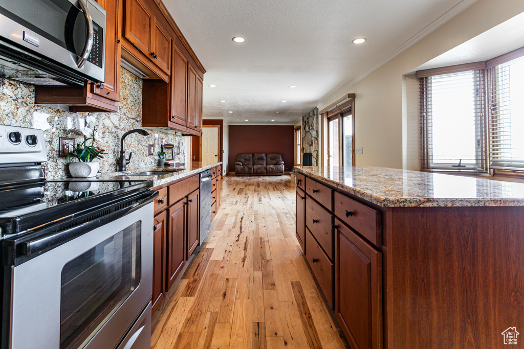 Kitchen with stainless steel appliances, a sink, backsplash, light wood finished floors, and crown molding
