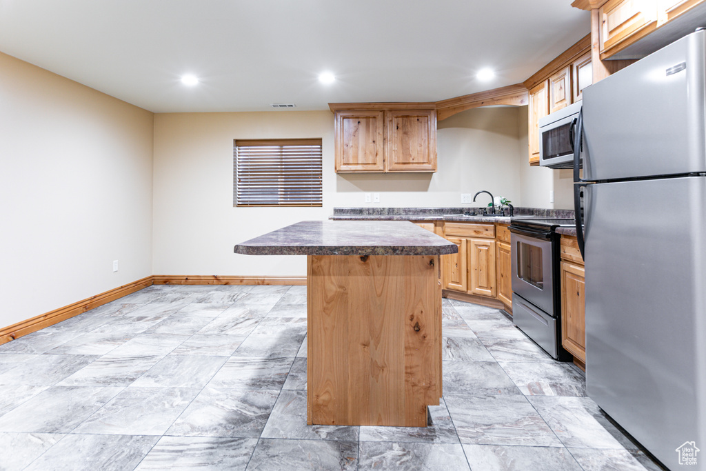 Kitchen with stainless steel appliances, a kitchen island, recessed lighting, dark countertops, and light brown cabinetry