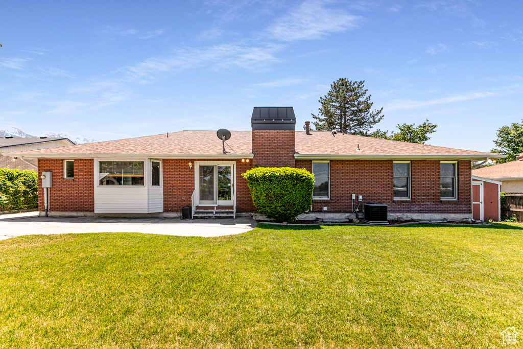 Back of property featuring entry steps, a patio area, a yard, brick siding, and a chimney