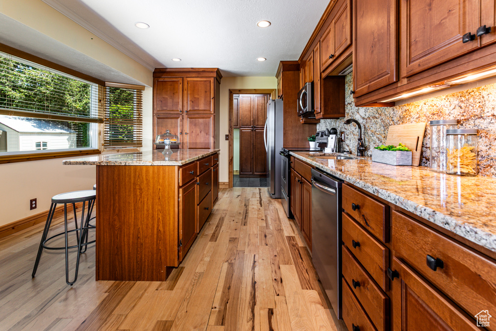 Kitchen with appliances with stainless steel finishes, a center island, light wood-style floors, a breakfast bar, and brown cabinetry