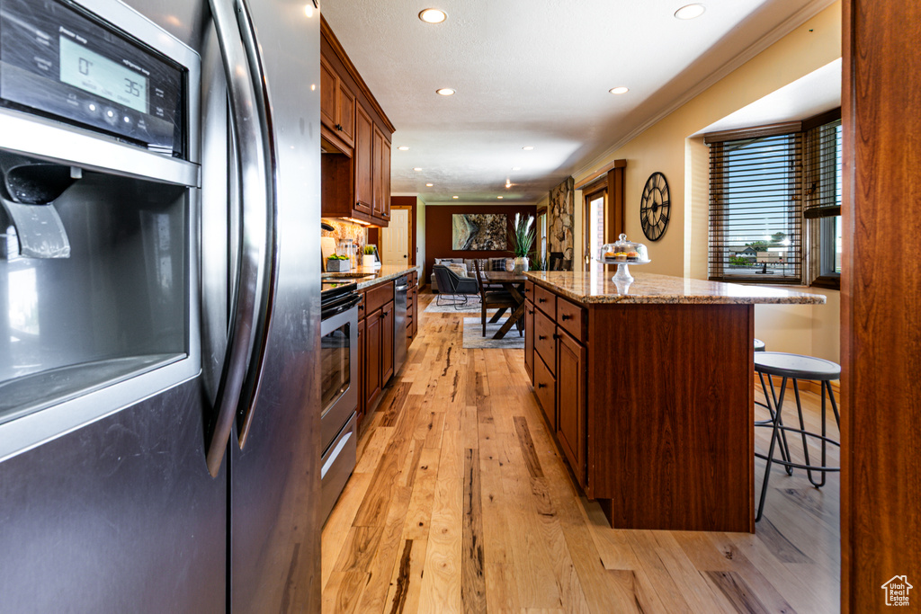 Kitchen with stainless steel appliances, a kitchen island, a kitchen bar, recessed lighting, and light wood-style floors