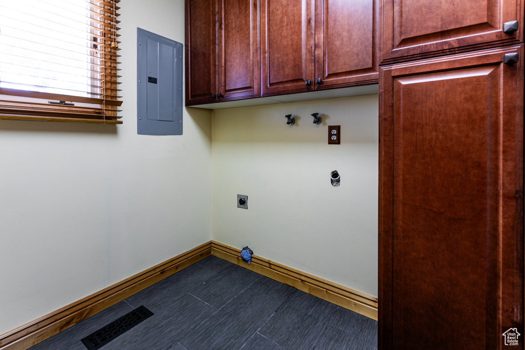 Laundry room with hookup for an electric dryer, electric panel, cabinet space, and baseboards