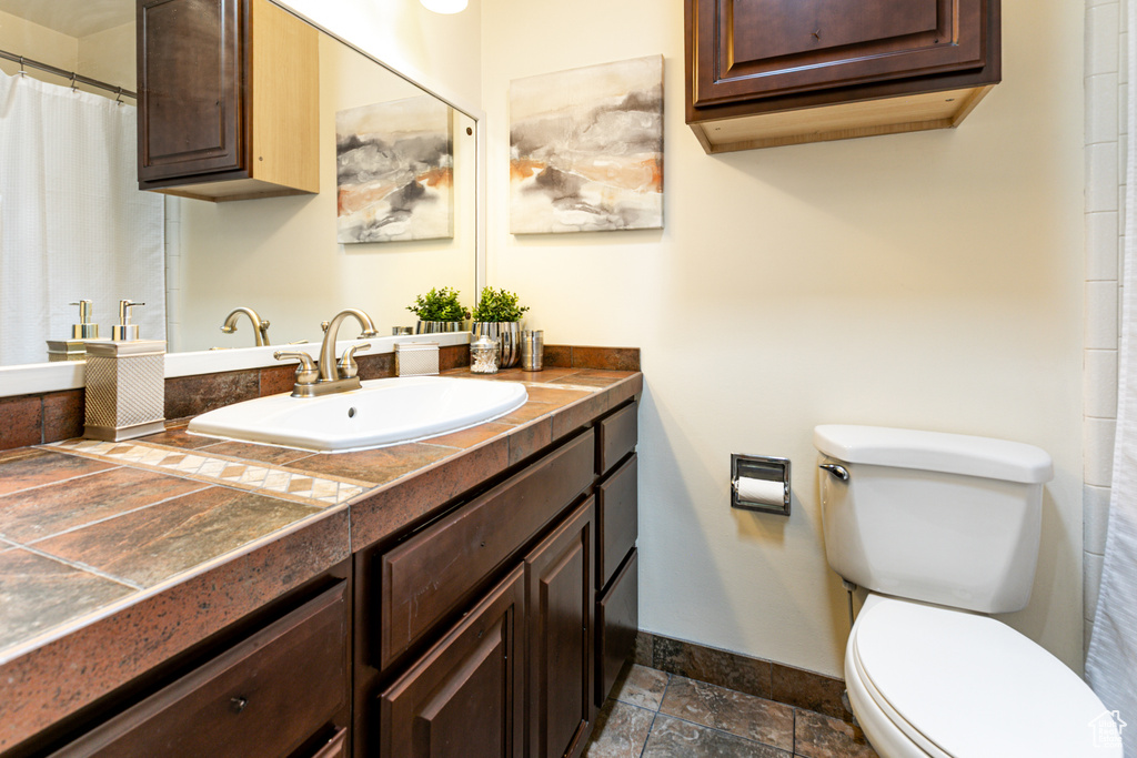 Bathroom featuring baseboards, vanity, toilet, and stone tile flooring