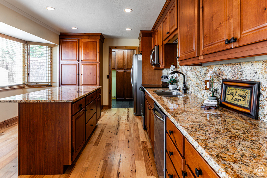 Kitchen featuring stainless steel appliances, a sink, a center island, decorative backsplash, and light wood finished floors