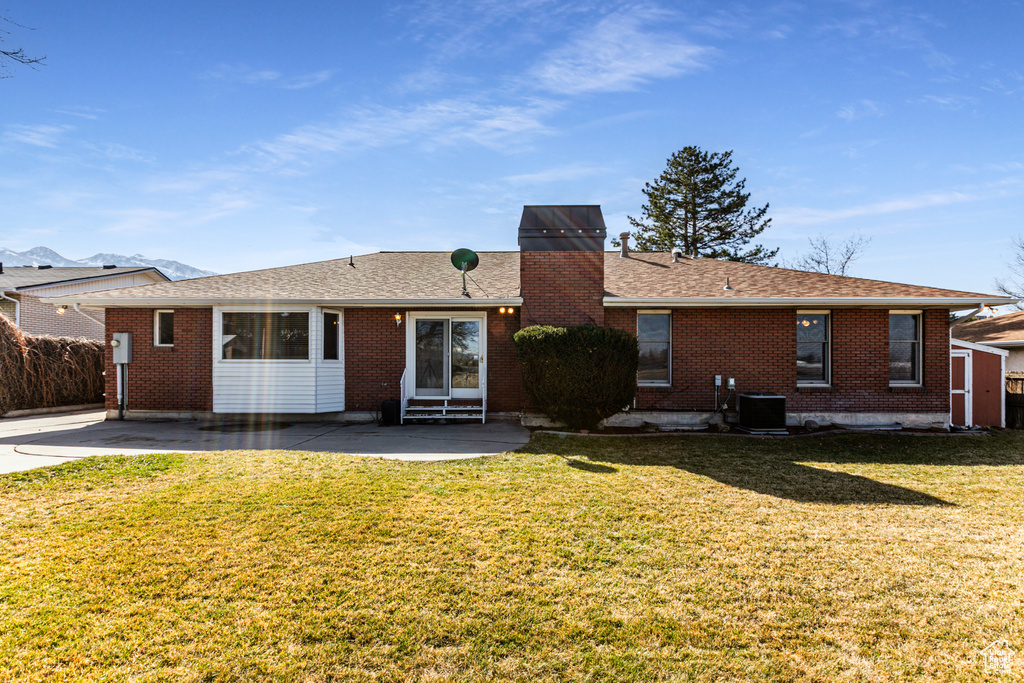 Back of property featuring a yard, brick siding, central AC, and a chimney