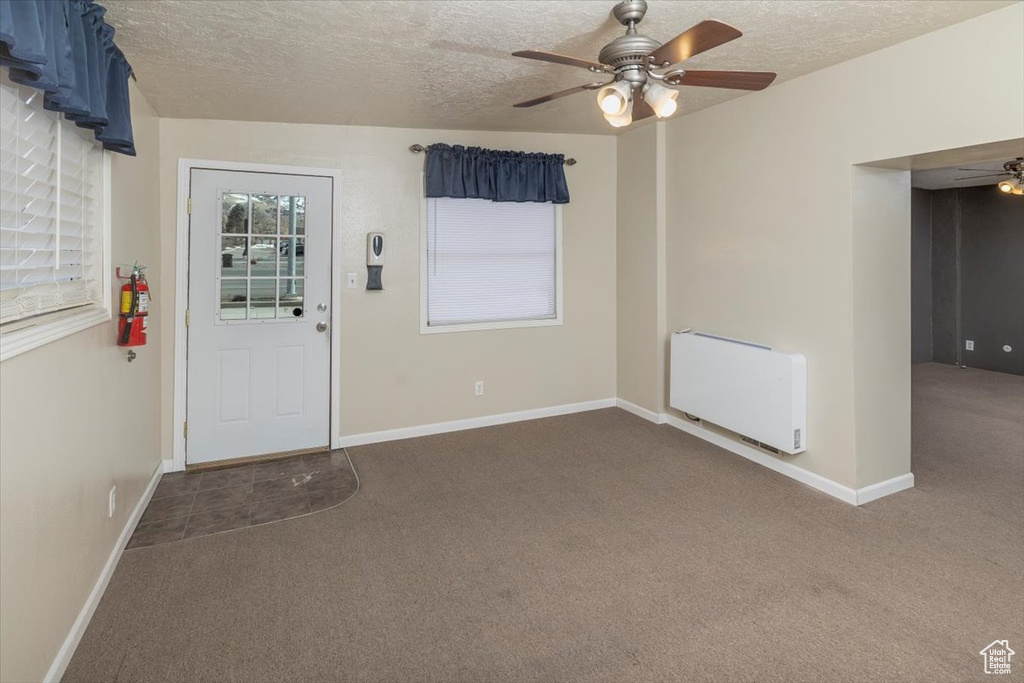 Carpeted entrance foyer featuring ceiling fan, a textured ceiling, baseboards, and radiator