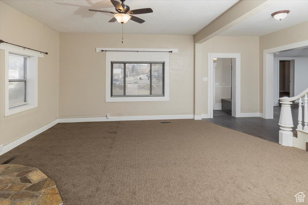 Unfurnished living room featuring a ceiling fan, dark carpet, and baseboards