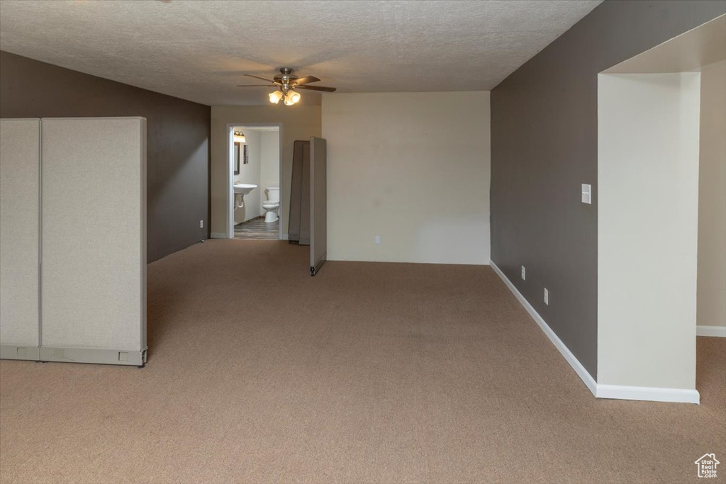 Carpeted spare room featuring a textured ceiling, ceiling fan, and baseboards