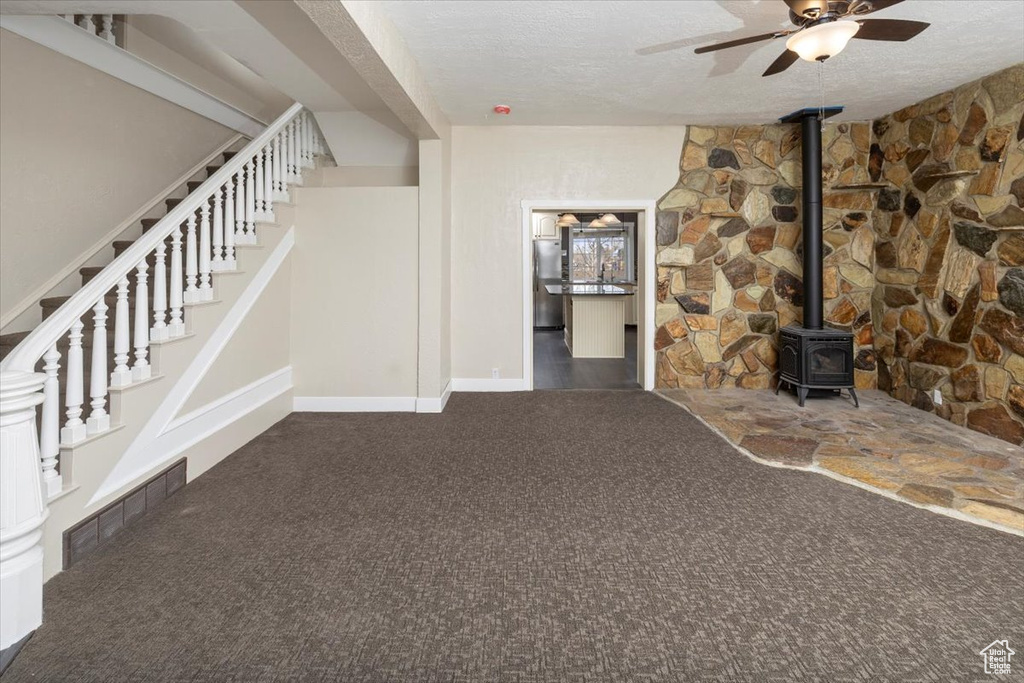 Unfurnished living room with a textured ceiling, carpet flooring, visible vents, stairs, and a wood stove