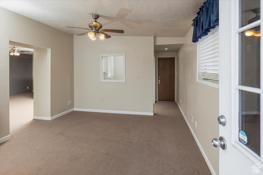 Carpeted empty room with a textured ceiling, ceiling fan, and baseboards