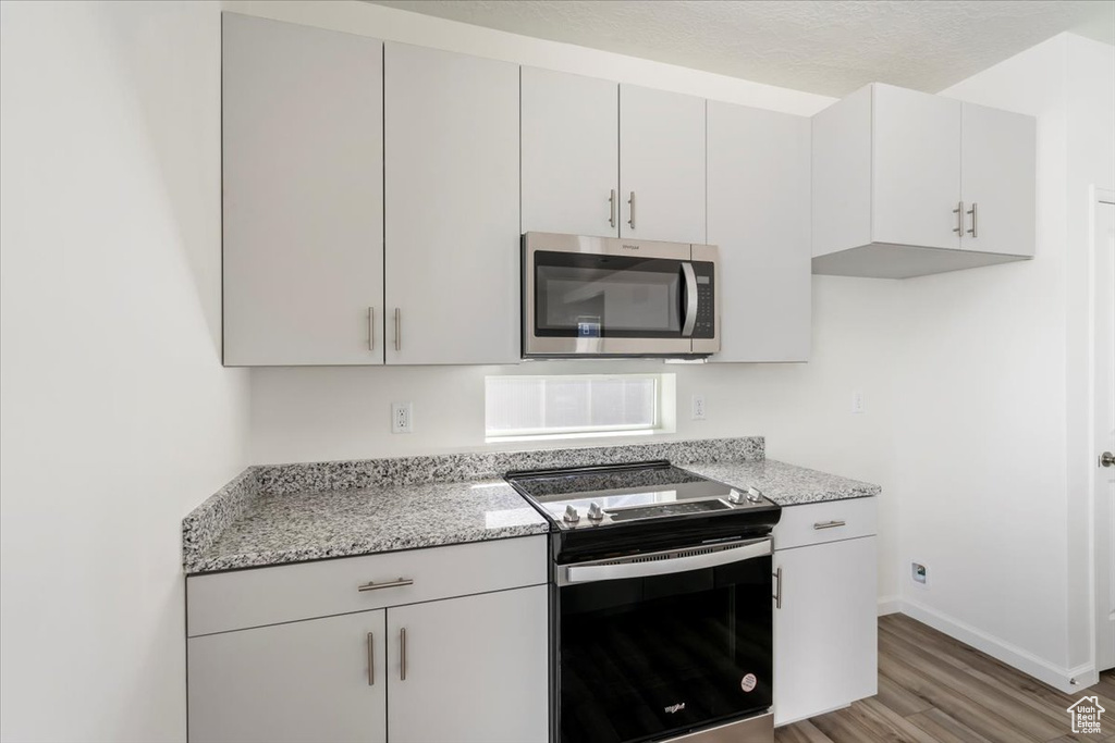 Kitchen with light stone countertops, light wood-style flooring, appliances with stainless steel finishes, and baseboards