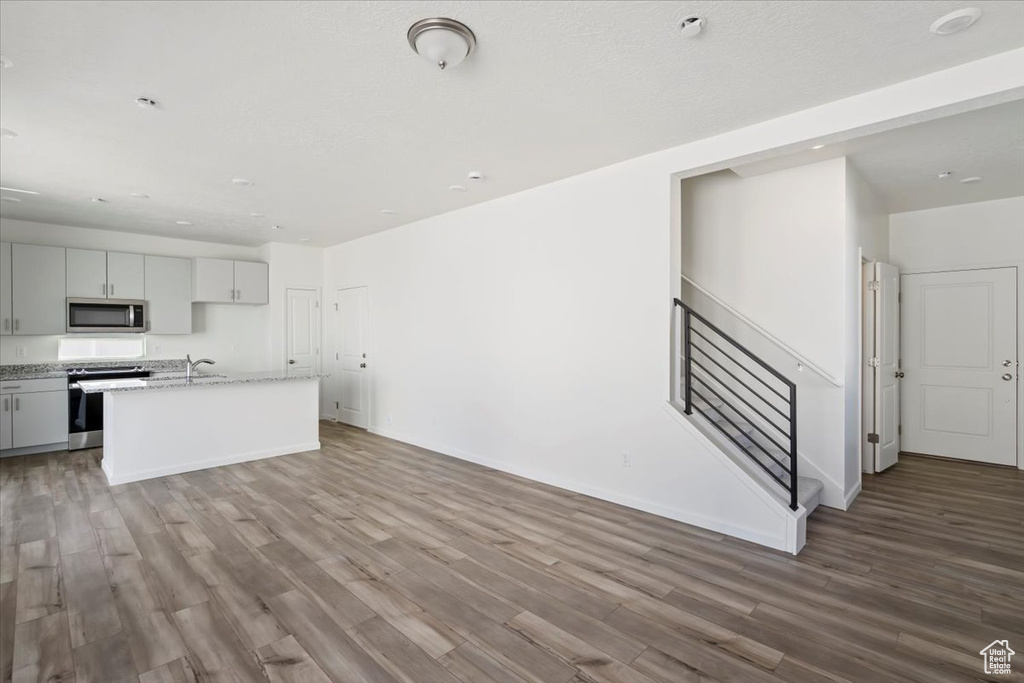 Kitchen with range, stainless steel microwave, wood finished floors, a kitchen island with sink, and a sink