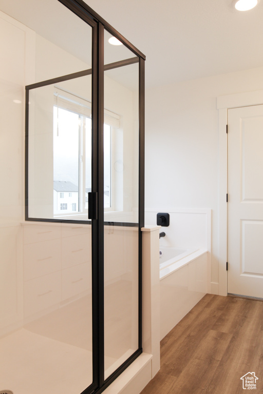Bathroom with wood finished floors, a garden tub, and a shower with shower door