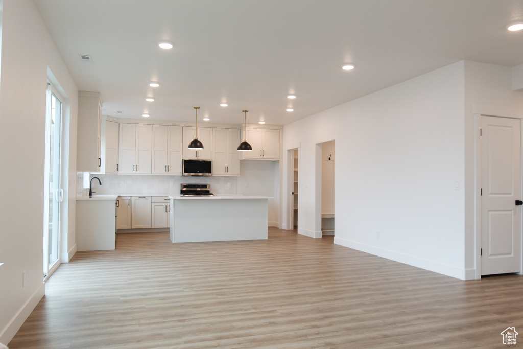 Kitchen featuring stainless steel appliances, light wood-style floors, open floor plan, tasteful backsplash, and baseboards