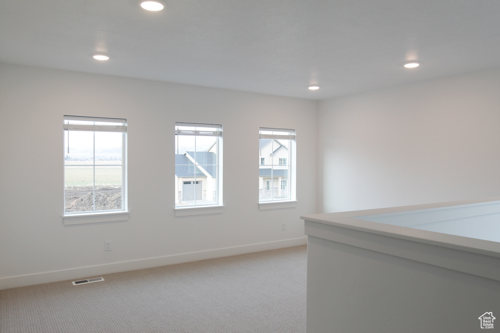 Empty room featuring healthy amount of natural light, light colored carpet, recessed lighting, and baseboards