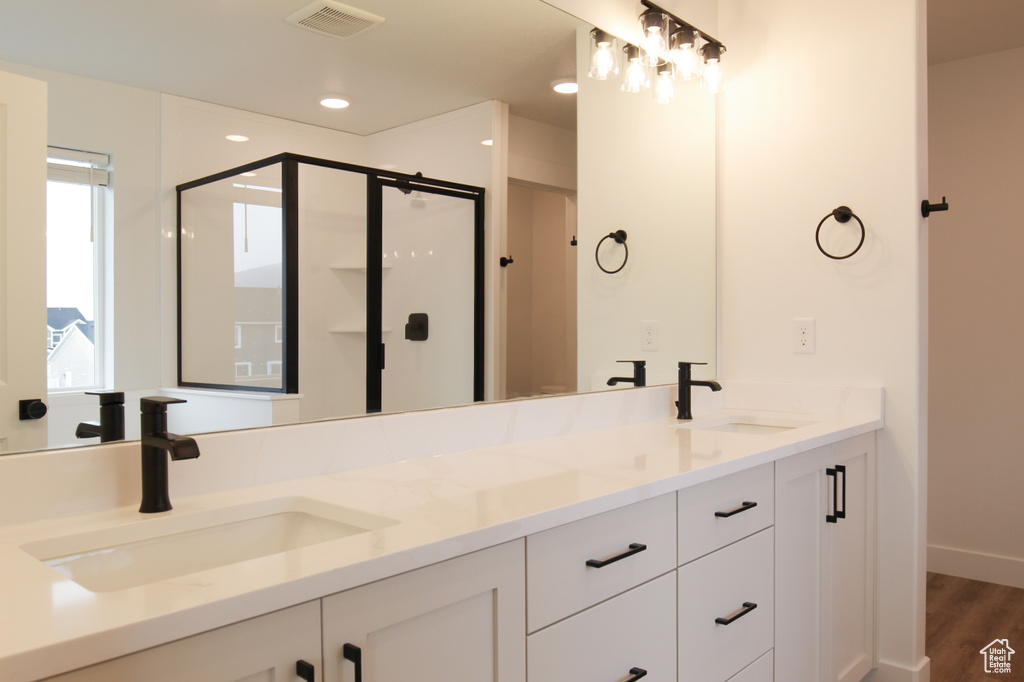Full bathroom with a shower stall, double vanity, wood finished floors, and recessed lighting