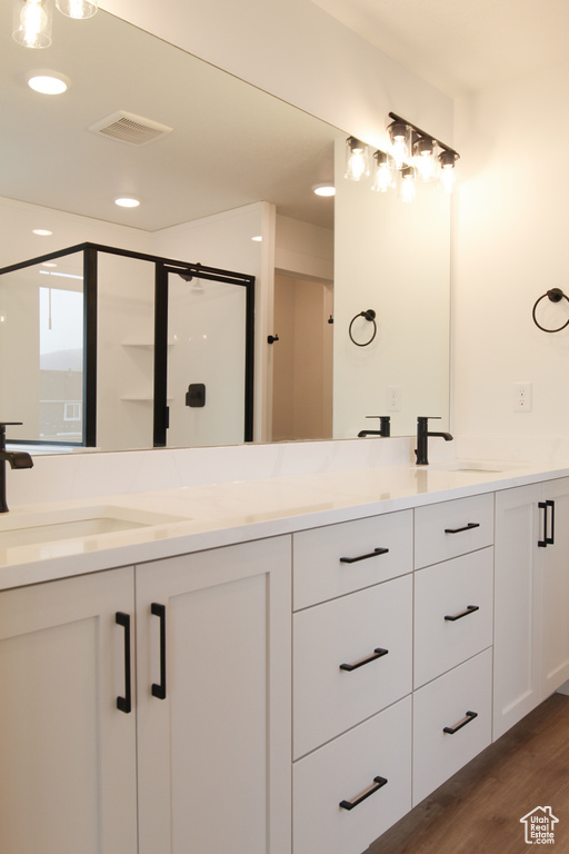 Bathroom with wood finished floors, double vanity, a stall shower, and recessed lighting