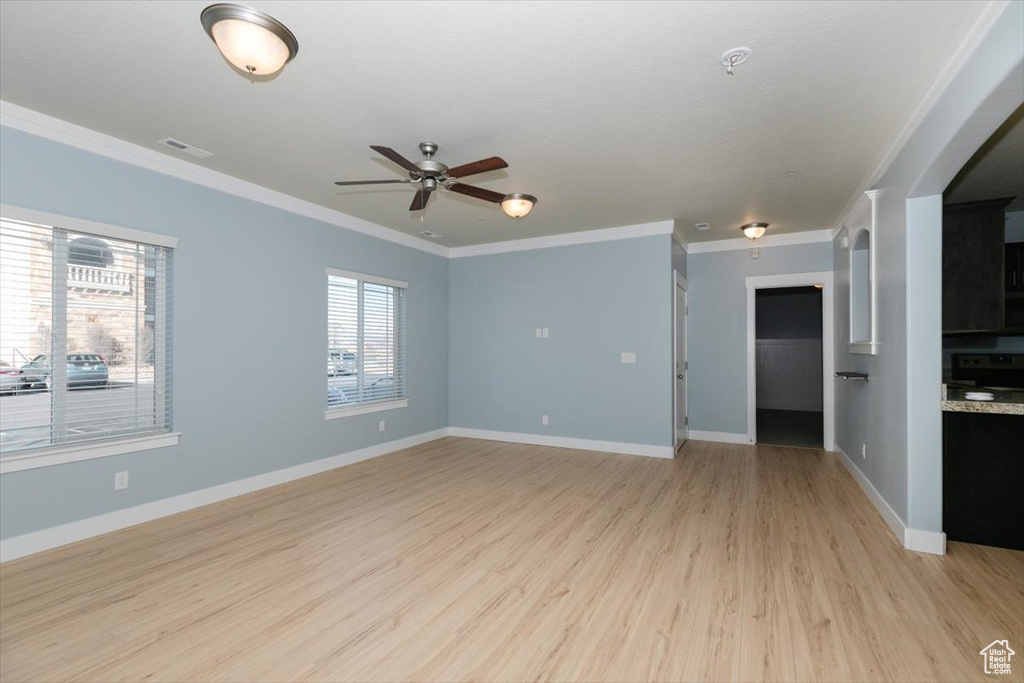 Spare room with crown molding, light wood-style flooring, baseboards, and visible vents