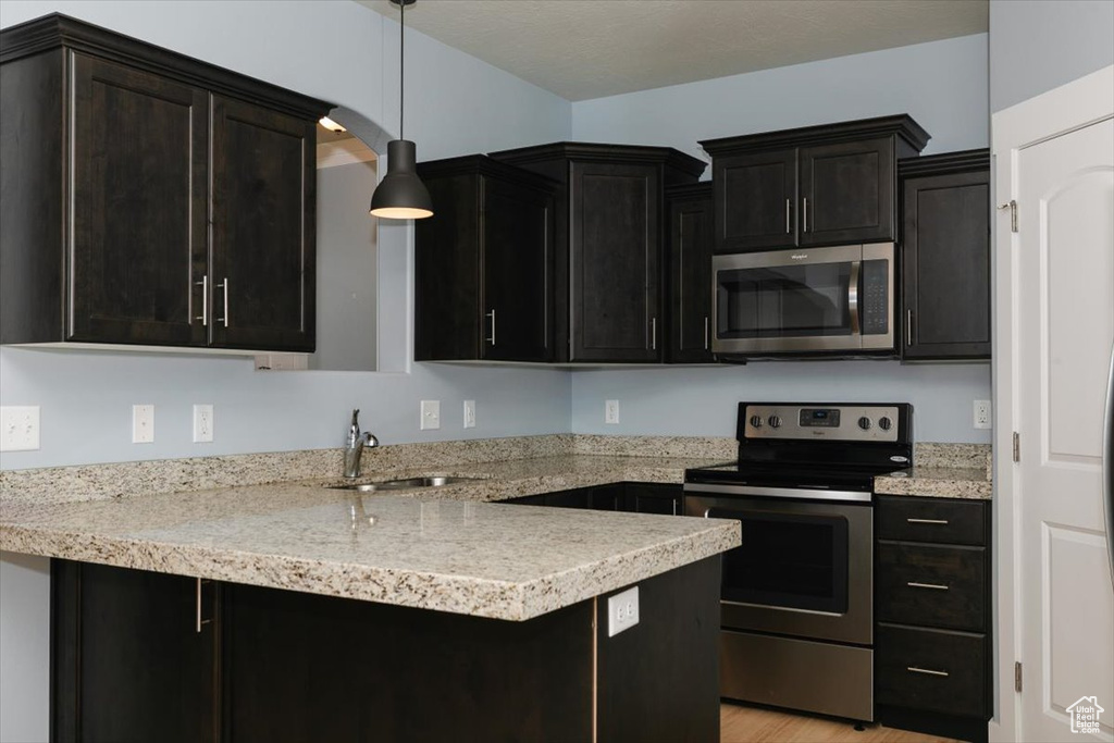 Kitchen featuring a sink, decorative light fixtures, a peninsula, stainless steel appliances, and dark cabinets