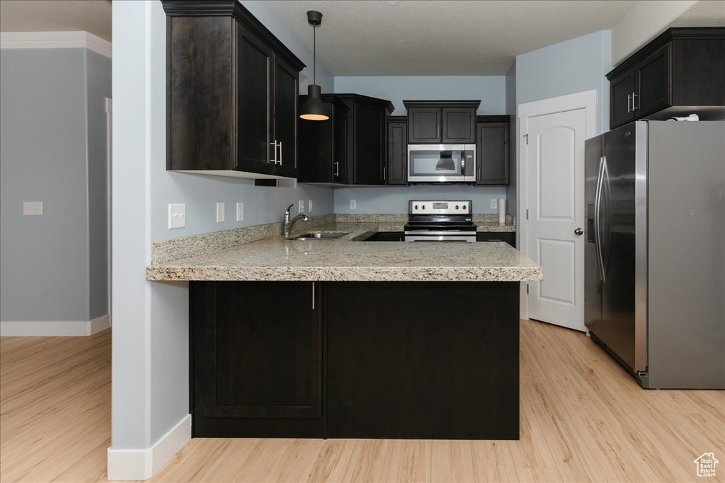 Kitchen with pendant lighting, a sink, light wood-style floors, appliances with stainless steel finishes, and a peninsula