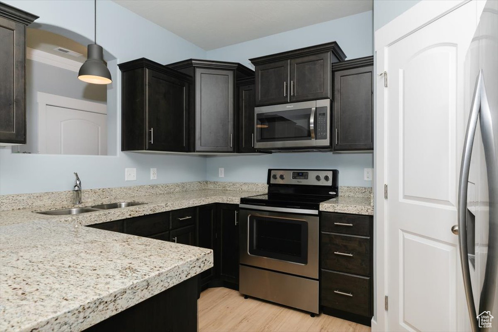 Kitchen with pendant lighting, a sink, stainless steel appliances, light wood finished floors, and light stone countertops