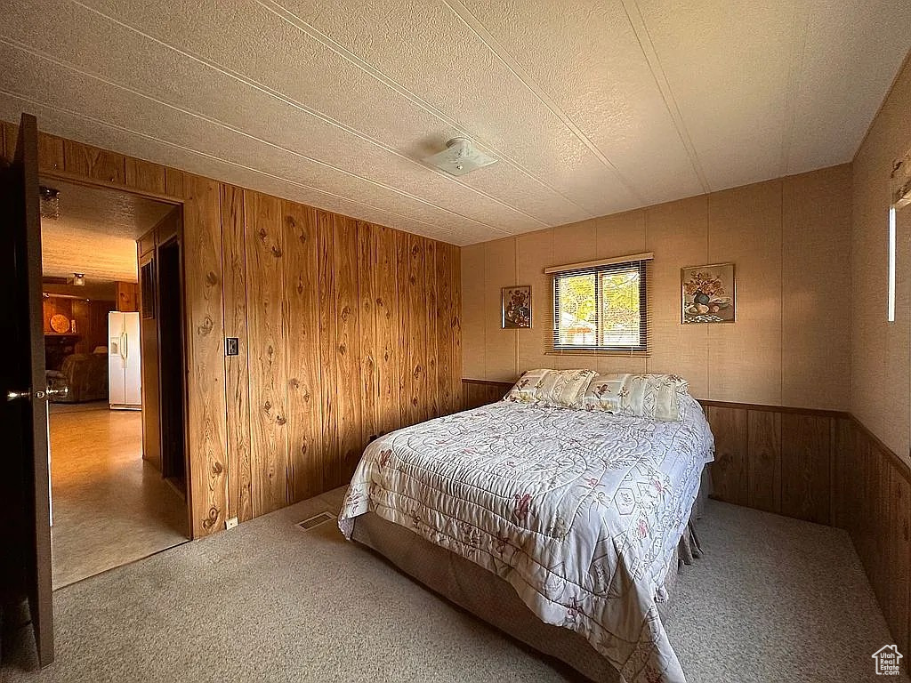 Carpeted bedroom featuring white refrigerator with ice dispenser and wood walls