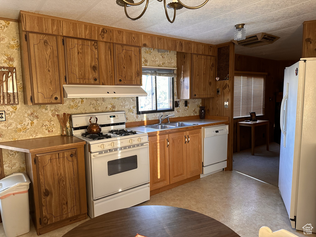 Kitchen with white appliances, under cabinet range hood, a sink, and wallpapered walls