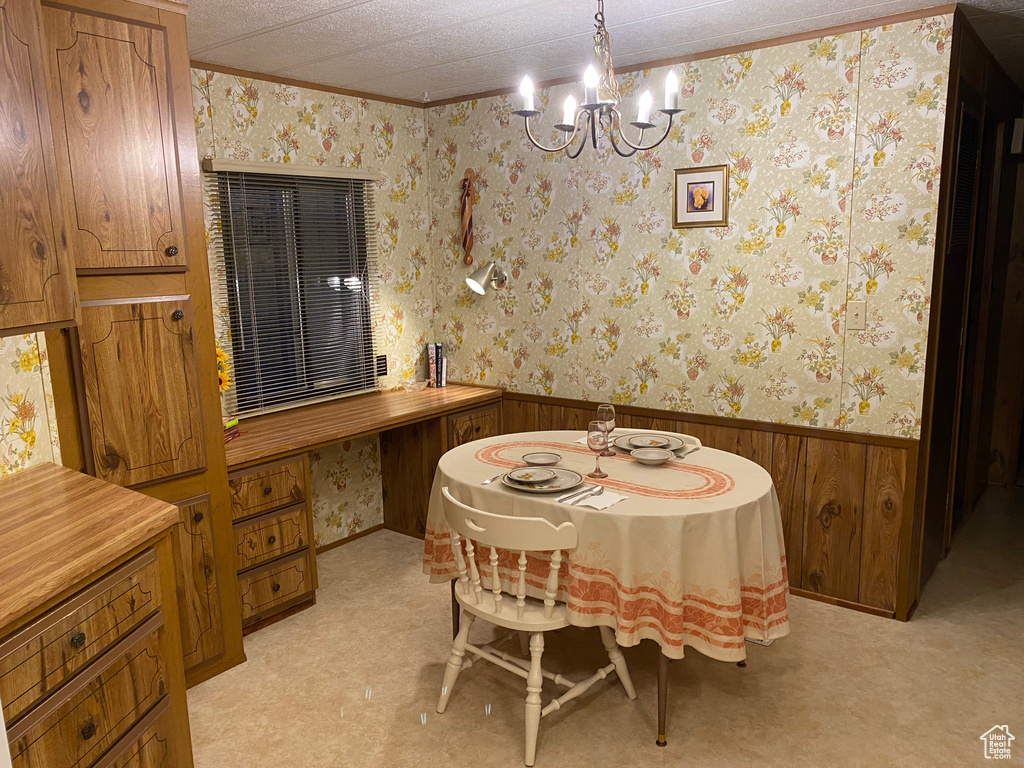 Dining room featuring wallpapered walls, a notable chandelier, a wainscoted wall, and light colored carpet
