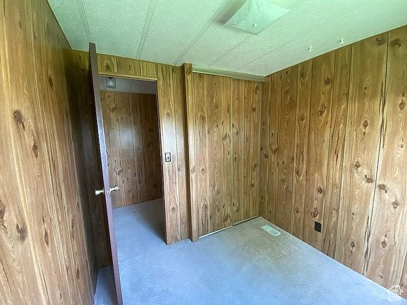 Unfurnished room featuring carpet flooring, visible vents, and wooden walls