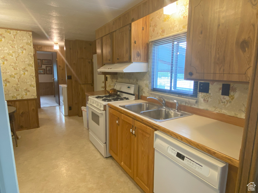 Kitchen featuring wallpapered walls, white appliances, wainscoting, under cabinet range hood, and a sink